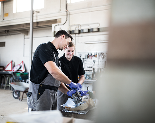 Zwei Männer in Arbeitskleidung und Handschuhen untersuchen Materialien in einer Industrieanlage.