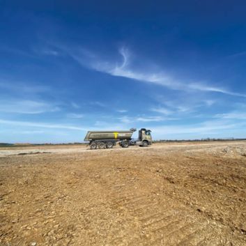 Unter einem klaren blauen Himmel fährt ein LKW auf einem weiten, kargen Feld.