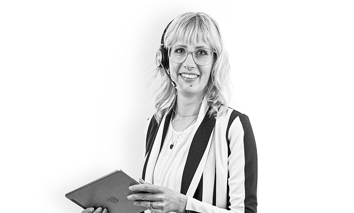 Person mit Brille und Headset, hält ein Tablet und lächelt vor einem einfarbigen Hintergrund.